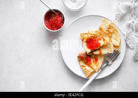 Crepe sottili con caviale rosso e crema servite su sfondo bianco, vista dall'alto, spazio copia. Pancake salati con caviale di pesce salmone. Carnevale di Maslenitsa. Foto Stock