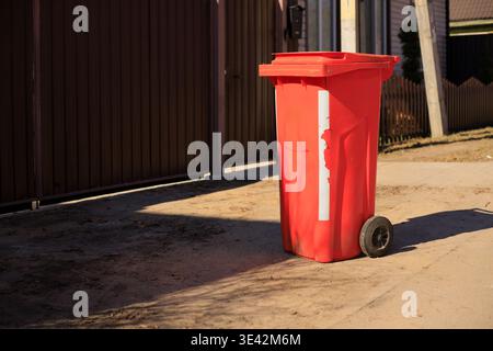 Contenitore di plastica arancione per la spazzatura in piedi per strada al tramonto. Foto Stock