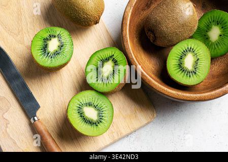 Frutta kiwi in una ciotola di legno. Frutta intera e mezzo pezzetti di kiwi verde da vicino. Kiwi maturo fresco. Alimentazione sana organica. Foto Stock