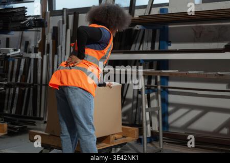 Donna addetto alla logistica e al magazzino che soffre di mal di schiena dopo la movimentazione manuale, il sollevamento e il trasporto di pesanti scatole di cartone. Foto Stock