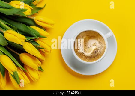 Caffè su sfondo giallo con tulipani gialli, brillante concetto primaverile Foto Stock