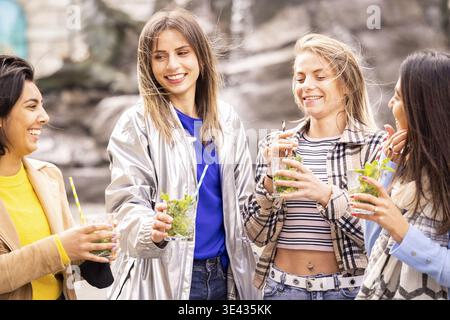 Un gruppo gioioso di amici che socializzano all'aperto, sorridono e sorseggiano un drink in un incontro positivo Foto Stock