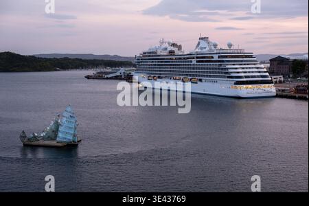 Oslo giace una scultura galleggiante nell'acqua del porto con una grande nave da crociera attraccata di sera, paesaggio urbano sullo sfondo. Norvegia Foto Stock