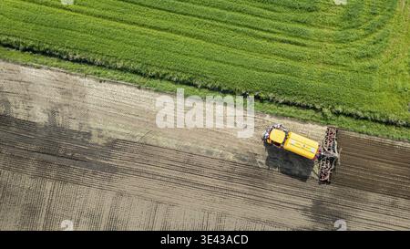 Un drone cattura riprese aeree di terreni agricoli con moderne attrezzature per trattori che lavorano su colture, mostrando l'agricoltura Foto Stock
