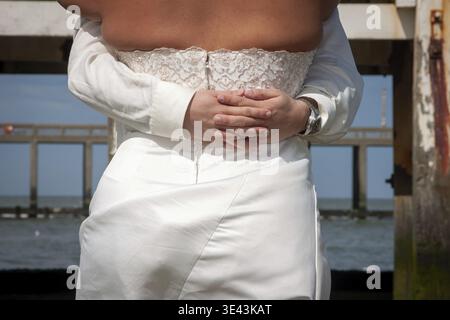 Una coppia vestita con un bellissimo abito da sposa condivide un abbraccio amorevole mentre si trova sulla spiaggia di sabbia Foto Stock