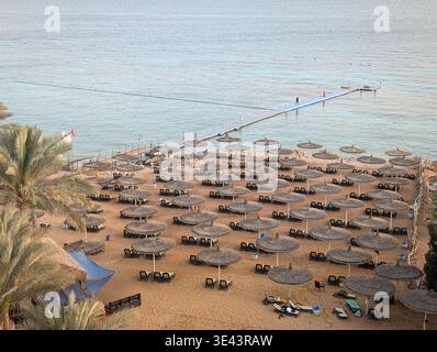 Vista aerea di una lussuosa spiaggia di sabbia a Sharm El Sheikh in Egitto con file di ombrelloni di paglia e lungo molo galleggiante. Foto Stock