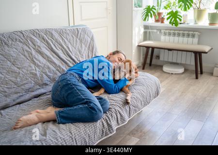 Donna matura positiva spensierata sdraiata sul divano coccolare con il cane Vizsla, mostra amore e calore per gli animali domestici. Foto Stock