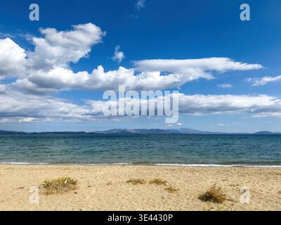 Spiaggia sabbiosa sulla costa dell'Attica sotto il cielo azzurro e nuvole alla deriva, mare calmo e surf dolce, canne sulla riva vicino a Marathon, Grecia Foto Stock