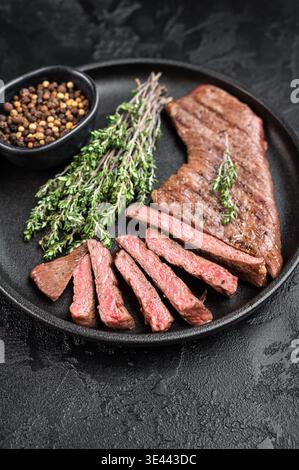 Bistecca di manzo a fette succose con erbe e pepe sul piatto, carne cotta con consistenza e fibre, pasto gourmet pronto da mangiare Foto Stock