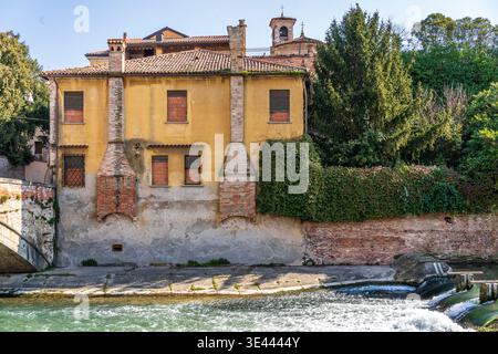 Affascinante casa gialla con enormi camini in mattoni lungo il fiume Bacchiglione a Padova. Sullo sfondo si trova la torre della chiesa di San Giovanni. A h Foto Stock