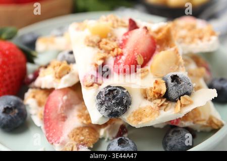 Pezzi di gustosa corteccia di yogurt con frutti di bosco e muesli sul tavolo, primo piano Foto Stock