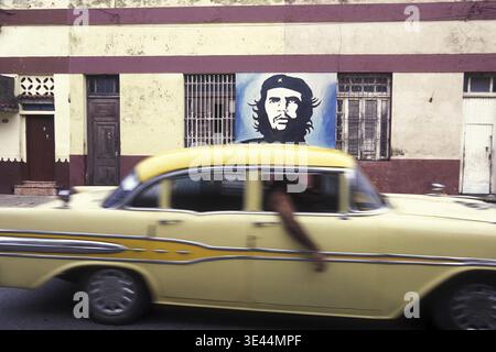 Una foto di che Guevara su un muro e di vecchie auto americane su una strada nella città di l'Avana a Cuba nel mare dei caraibi. Cuba, l'Avana, ottobre 2005 Foto Stock