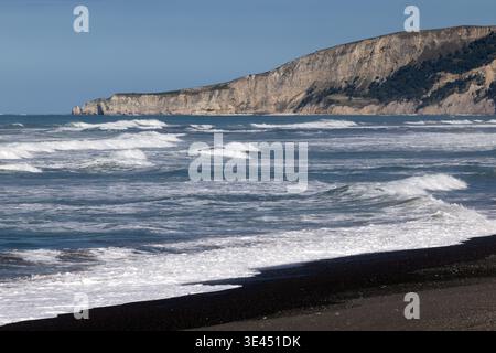 Onde che si infrangono sulla spiaggia di sabbia nera con scogliere costiere, Kaikōura, Canterbury, nuova Zelanda Foto Stock