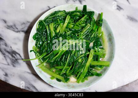 Spinaci d'acqua fritti in padella con aglio su piatto in ceramica in cucina cinese, Shanghai Foto Stock