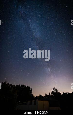 Bergnicourt, Rethel, Ardenne, Grand-Est, Francia, 28 agosto 2025, Galaxy sale sopra tranquilli quartieri residenziali, mostra celestiale oltre le case suburbane con un'accogliente illuminazione interna Foto Stock