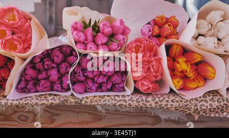Colorati mazzi di tulipani primaverili avvolti in carta per la vendita in un mercato di fiori Foto Stock