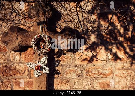Una croce di pietra ornamentale intemprata si appoggia graziosamente contro un muro antico in un cimitero storico. Le intricate incisioni sulla croce sono evidenziate Foto Stock