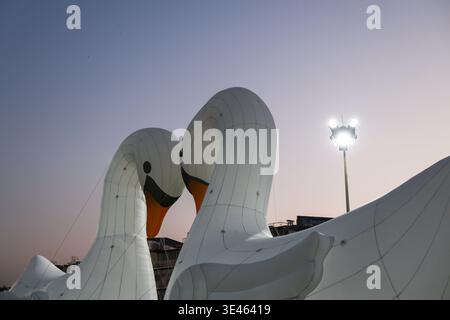 Grandi sculture bianche di cigno che si affacciano l'una sull'altra contro il cielo sereno con lampioni luminosi che emettono un caldo bagliore per una sensazione di romanticismo e tranquillità Foto Stock