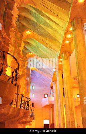 Interni della Sagrada Família, Barcellona: Luce arcobaleno che si lava sul soffitto in pietra piegata e alte colonne della navata laterale in tonalità oro e verde. Foto Stock