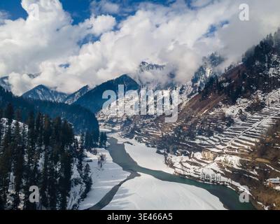 Vista aerea del tranquillo fiume che si snoda attraverso paesaggi innevati, villaggi annidati tra le maestose montagne, Sharda, Azad Kashmir, Pakistan Foto Stock