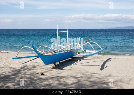 Vista laterale del Blue Outrigger boat sulla tranquilla spiaggia tropicale e sul mare cristallino Foto Stock