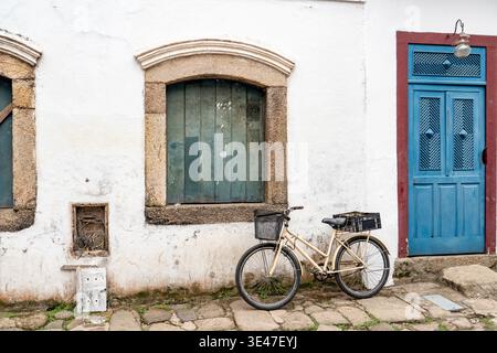 Bicicletta d'epoca parcheggiata da una porta colorata blu e da un muro coloniale bianco in Brasile Foto Stock