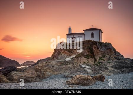 Piccola Cappella Bianca sulla scogliera rocciosa al tramonto su Rugged Coastal Beach e Calm Sea, Valdovino, Spagna Foto Stock