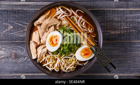 Giapponese ramen zuppa di pollo, uova, erba cipollina e il germoglio sul legno scuro dello sfondo. Foto Stock