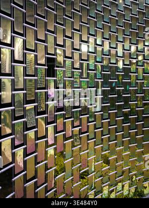 Parete esterna decorativa con numerose piccole piastrelle di vetro riflettente illuminate da luci calde di notte. La scena rappresenta l'architettura moderna Foto Stock