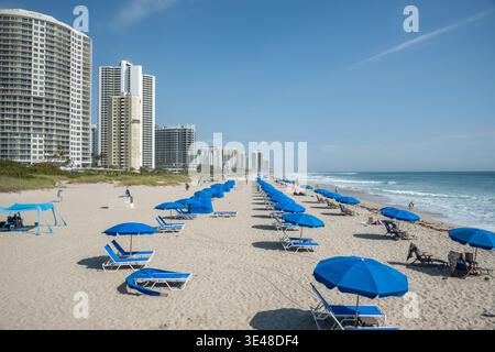 Riviera Beach, Florida, Stati Uniti – 26 marzo 2026: Spiaggia con ombrelloni blu, onde dell'oceano e appartamenti alti lungo la costa atlantica. Foto Stock