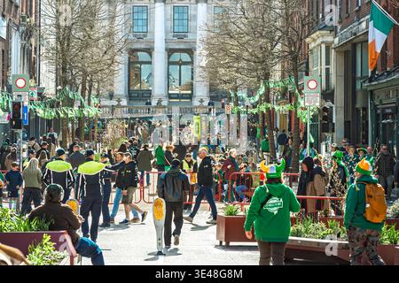 Folle festose e polizia di Garda su Parliament Street durante il festival di San Patrizio nel centro di Dublino, Irlanda. Foto Stock