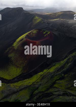 Vista aerea di un cratere vulcanico con suolo rosso e muschio verde circondato da un paesaggio vulcanico nero in Islanda. Foto Stock