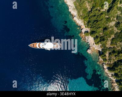 Vista aerea di uno yacht ormeggiato nelle acque turchesi lungo la costa rocciosa di Hvar, Spalato-Dalmazia, Croazia. Foto Stock