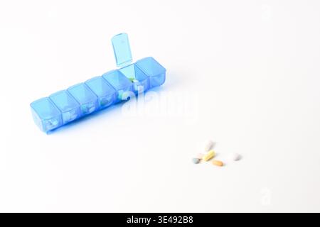 Organiser per pillole blu settimanale con scomparto aperto e pillole sfuse, isolato su bianco con spazio per copie. Foto Stock