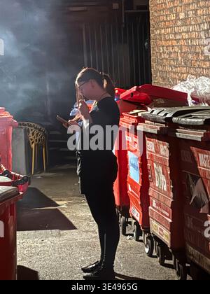 Una persona sta di fronte ai cassonetti rossi, guardando il telefono. Foto Stock
