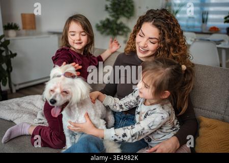 Una famiglia felice che si unisce al divano, accarezzando il loro amato cane Foto Stock