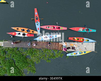 Vista aerea di canoe e kayak colorati raggruppati vicino a un molo di legno orlato da vegetazione verdeggiante, dia Bari Road, Dhaka, ঢাকা বিভাগ, Bangladesh. Foto Stock