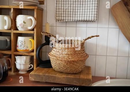 Affascinante cucina con cesto intrecciato tra tazze da tè e ripiani in legno rustico Foto Stock