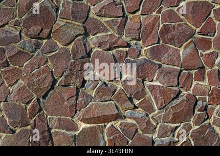 Sfondo irregolare della trama del muro di pietra marrone. Vista ravvicinata di un muro di pietra naturale irregolare con rocce marroni e rossastre, che creano una muratura robusta Foto Stock