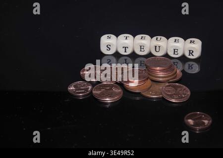 Parola Steuern (tasse) sui dadi di legno con monete da centesimo euro su sfondo nero Foto Stock