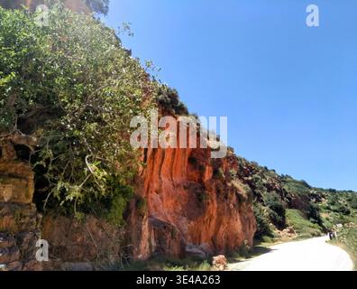 Montagna rocciosa rossa lungo una strada rurale in Marocco, che mostra una straordinaria geologia naturale e calde tonalità di terra. Un paesaggio aspro e panoramico Foto Stock