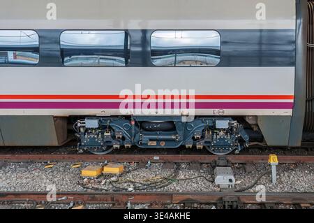 Primo piano di un lato della carrozza ferroviaria Renfe alla stazione di Valladolid-campo grande, che mostra l'assemblaggio del carrello ruota e l'infrastruttura dei binari. Foto Stock