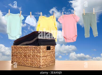 Cestino per bucato con abiti puliti sul tavolo. Indumenti che si asciugano contro il cielo Foto Stock