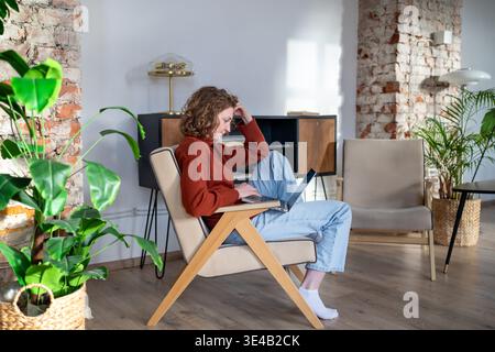 Donna dedicata e concentrata comfort online freelance che lavora con un notebook a casa pensando a idee creative Foto Stock