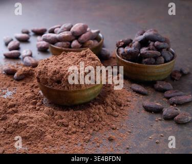 Fagioli di cacao e un mucchio di cacao in polvere in ciotole di legno su un tavolo di pietra Foto Stock