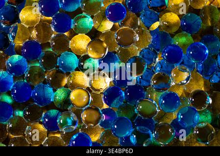 Vista ad alto angolo di molte perle colorate di gel d'acqua con riflessi blu e verdi nei dettagli macro. Foto Stock