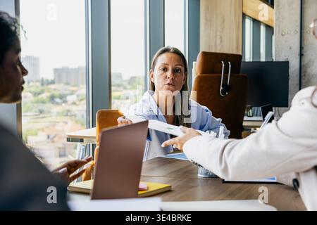 Donna che esamina i documenti. La donna si concentra sul rapporto mentre il coordinatore offre i documenti di approvazione nelle vicinanze Foto Stock