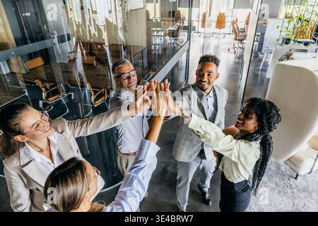 Colleghi felici si uniscono per festeggiare attorno al tavolo delle conferenze Foto Stock