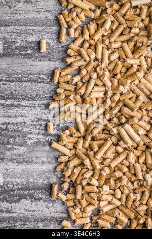Piccoli pellet di legno dorato sparsi su una superficie di cemento testurizzato, che rappresentano combustibile da biomassa, riscaldamento rinnovabile, combustibile per stufe ed energia sostenibile Foto Stock