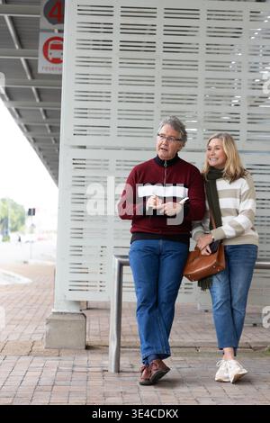 Coppia senior in piedi alla fermata coperta dell'autobus con notebook e penna con borsa in pelle e spazio per fotocopie Foto Stock